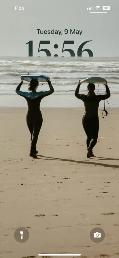 Two people walking on a beach carrying surfboards