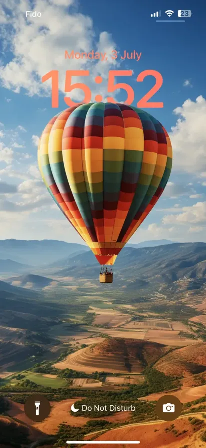 Colorful, patterned hot air balloon drifts under a bright blue sky, casting a charming shadow on the ground.