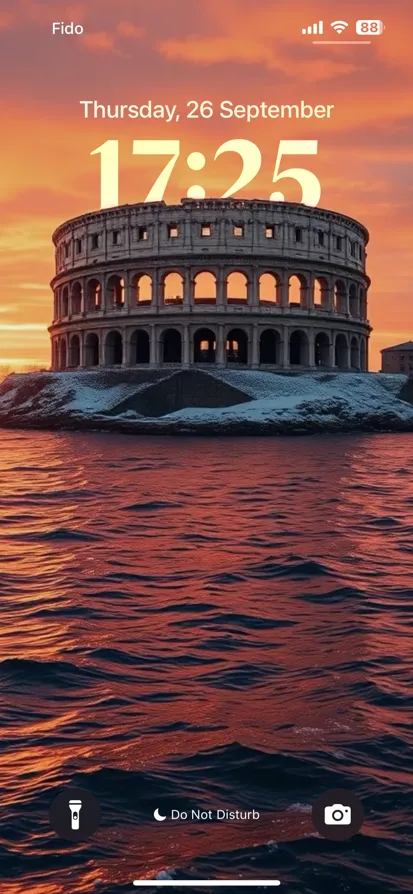 A vibrant sunset reflects in water near a historic amphitheater.